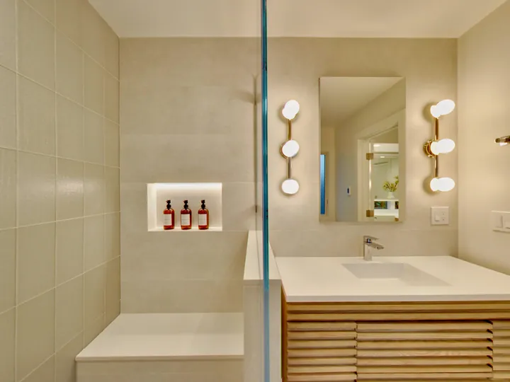 Bathroom with a lit shower niche, wall sconces and a slatted wood vanity