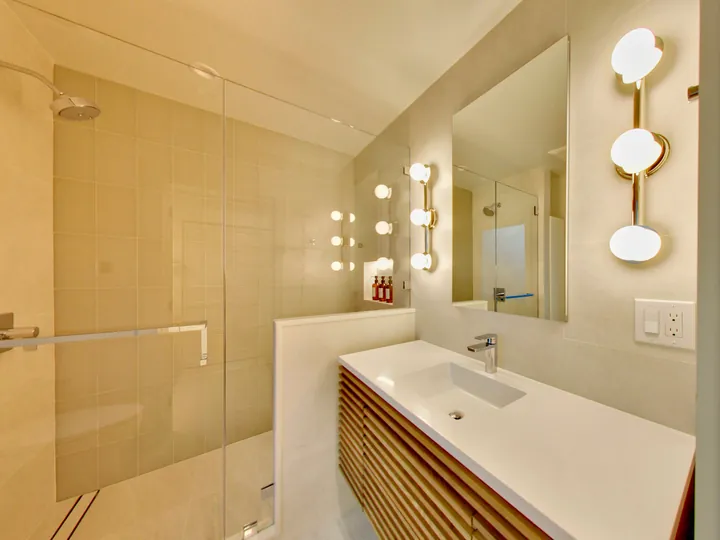 Slatted wood vanity with globe sconces and a glass shower panel